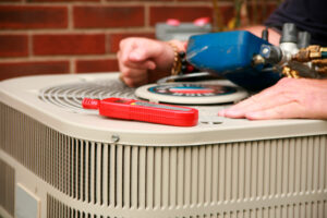 An HVAC technician works on an air conditioner unit beside a brick home.