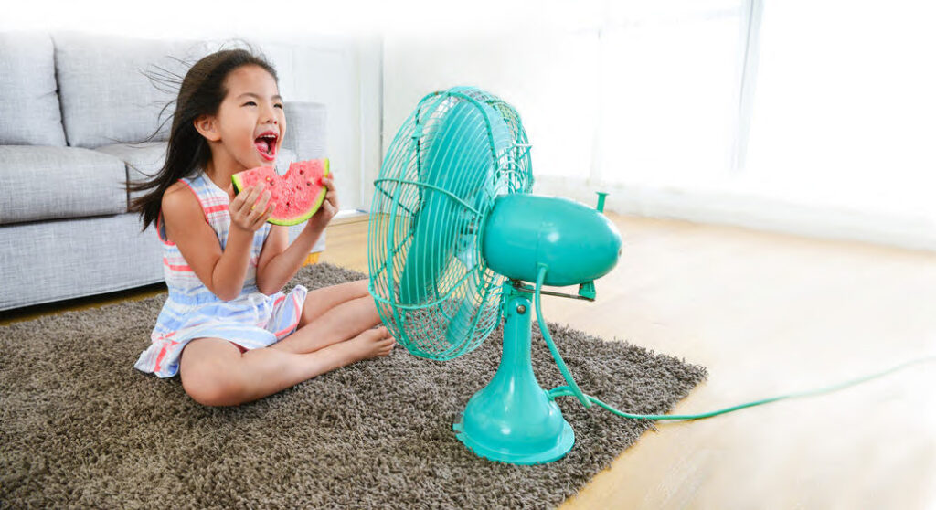 girl sitting in front of electric fan